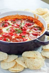 Pizza Dip Topped with Tomatoes and Parsley in Round Purple Dish surrounded by nacho chips.