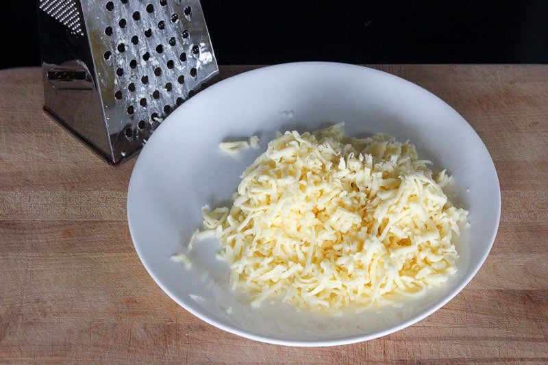 Plate of shredded mozarella cheese on cutting board with box grater.