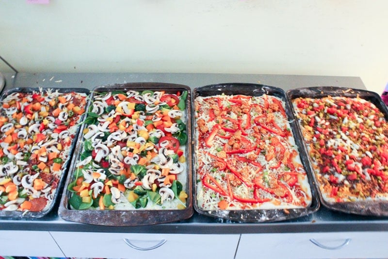 Adding Toppings to Four Pizzas in Rectangular Sheet Pans.