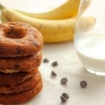 Stack of chocolate chip donuts with bananas and glass of milk.