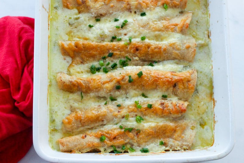 White pan with white enchiladas in it, and red cloth.