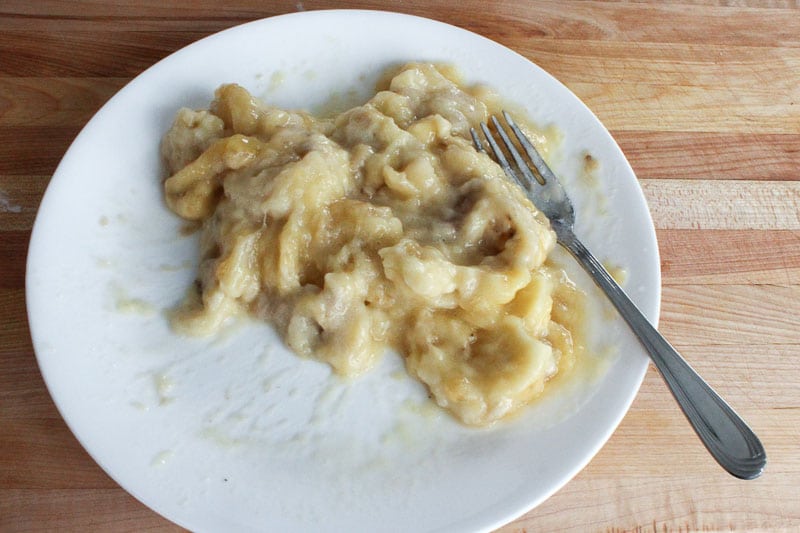 Mashed banana and fork on white plate.