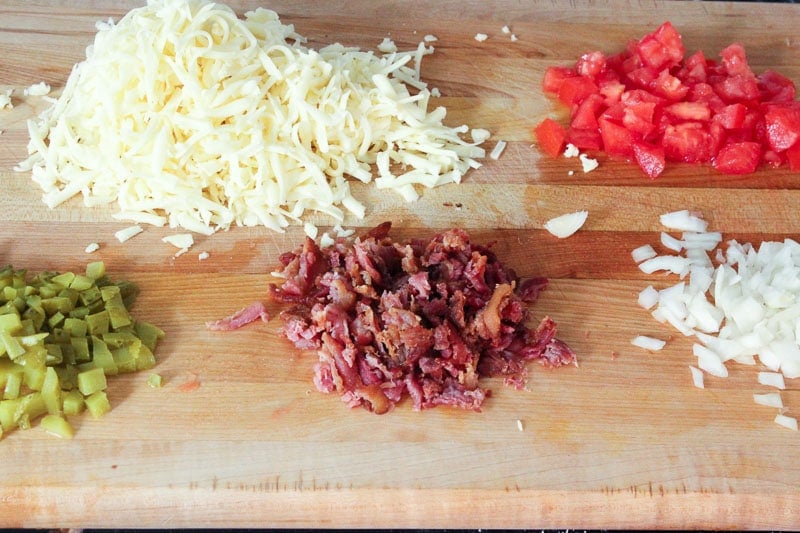 Shredded Mozzarella cheese, Chopped tomato, dill pickles, bacon and onion on Wooden Board.