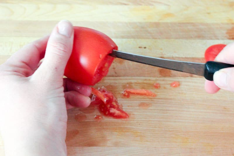 Using Knife to Scrape out tomato pulp from inside tomato.