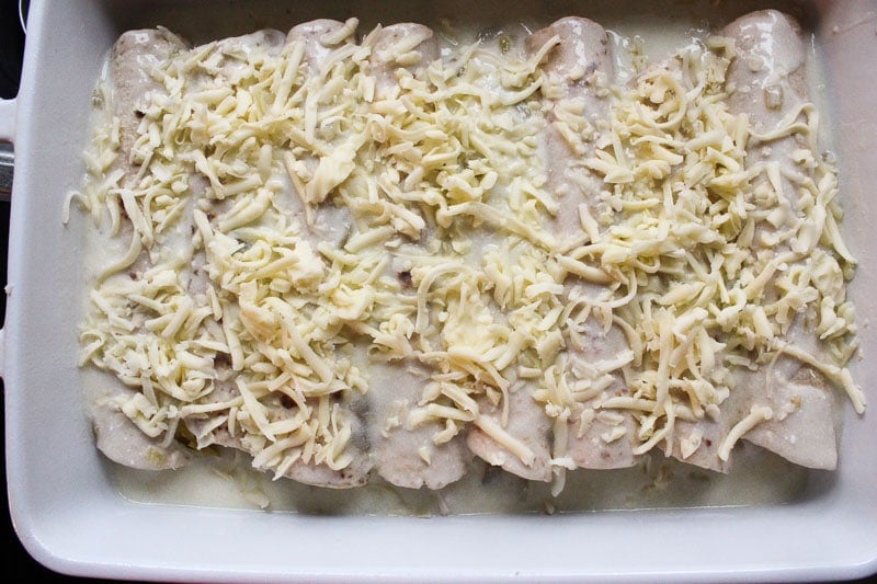 Tortillas rolled up in white Baking Dish, topped with White Sauce and Shredded Mozzarella Cheese.