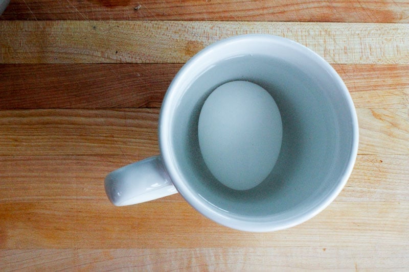 Egg in Mug Filled with Water on Wooden Board.