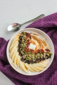 Yogurt, Sliced Banana, Nuts, Seeds, Raisins and Peanut Butter in White Bowl.