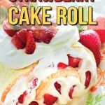 White cake roll, stuffed with whipped cream and sliced strawberries, with whipped cream, and sliced strawberries on top, garnished with mint leaves, on a colourful platter. Plates and forks in the background.