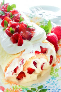 Easy Strawberry Cake Roll on a platter, topped with whipped cream and strawberries