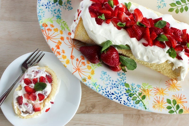 Slice of Strawberry Cake Roll Topped with Whipping Cream and Chopped Strawberries.