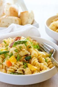 Bowl of creamy fusilli pasta with bell peppers, green beans and fresh herbs.