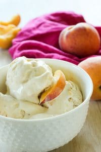 Peach ice cream topped with peach slice in a white bowl.