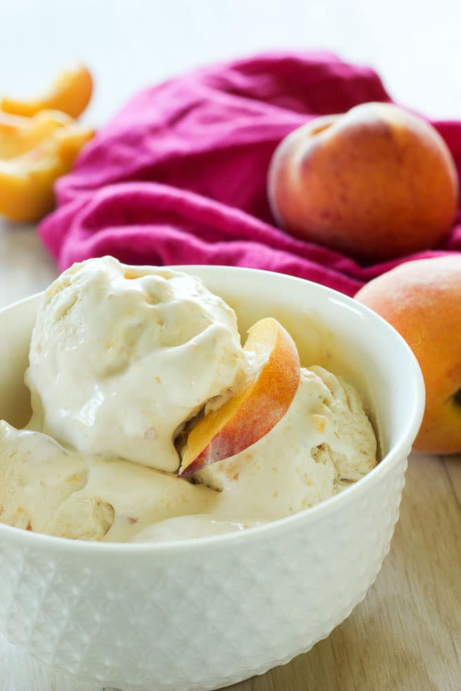 Peach ice cream topped with Peach Slice in a white bowl.