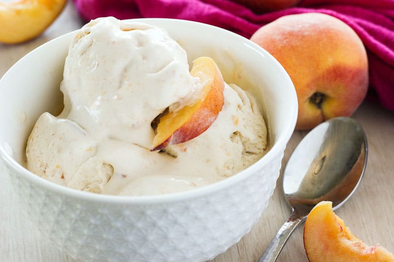 Peach ice cream topped with Peach Slice in a white bowl.