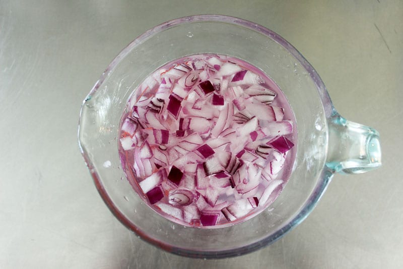 Chopped Red onion soaking in water in glass measuring cup.