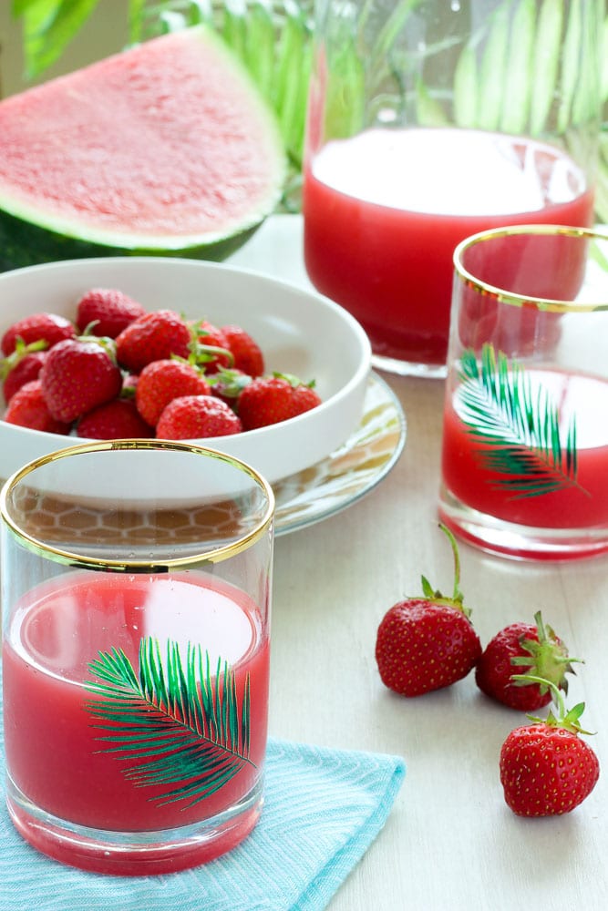 Strawberry Watermelon Juice in Glasses with bowl of Strawberries and Watermelon in background.