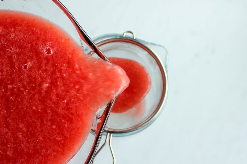 Watermelon and strawberry puree being poured through a sieve