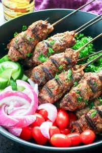 Ground beef kebabs on skewers, with grape tomatoes, red onion and cucumbers