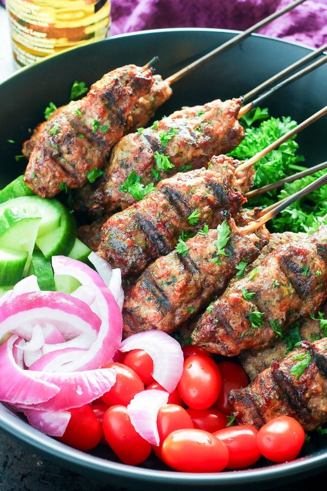 Beef kebabs on skewers, with grape tomatoes, red onion and cucumbers in Serving Dish.