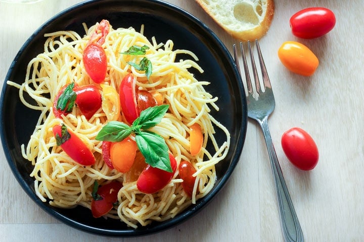 Pasta with fresh tomato sauce topped with fresh basil on black plate.