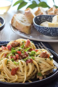 Pasta with sausage and bacon on black plate.