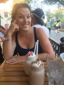 A woman smiling sitting at a table with milkshakes in front of her.