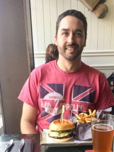 A man smiling sitting in front of a burger and fries.