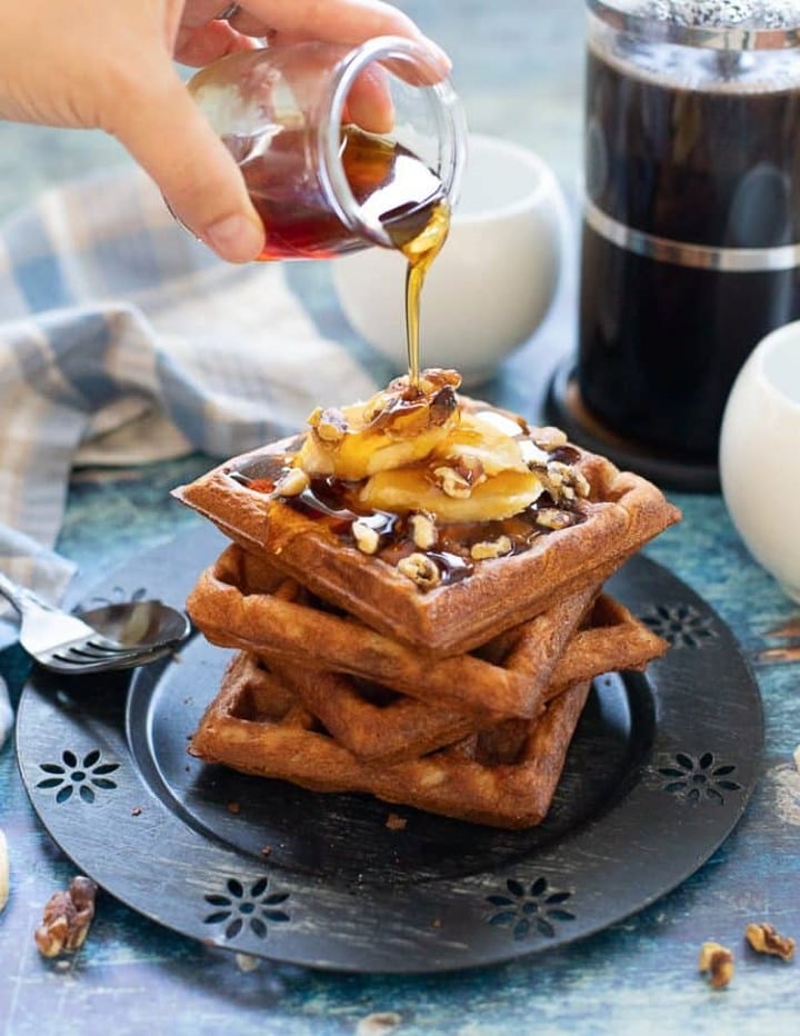Cup drizzling maple syrup over a stack of waffles