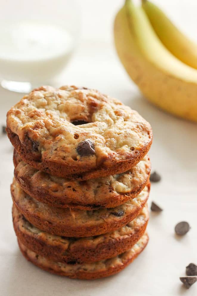 Stack of banana chocolate chip donuts, with a glass of milk and bunch of bananas