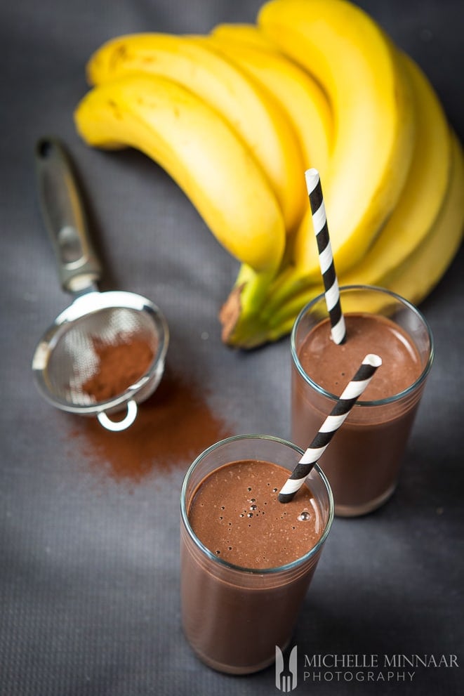 Glasses of chocolate banana protein shake with bunch of bananas