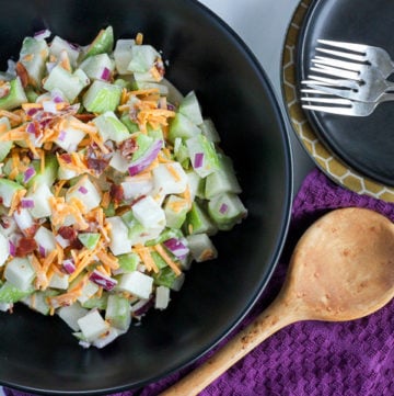 Chayote salad in black serving bowl, with side plates and forks