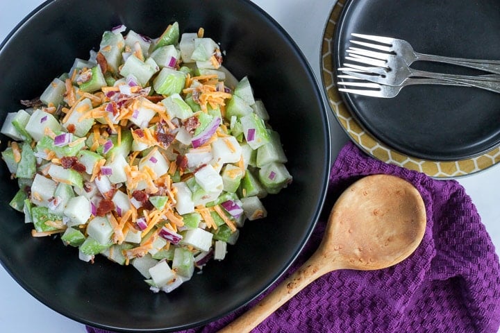 Chayote salad in black serving bowl, with side plates and forks