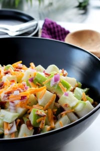 Large black bowl full of creamy chayote squash salad with bacon, cheddar cheese and onions