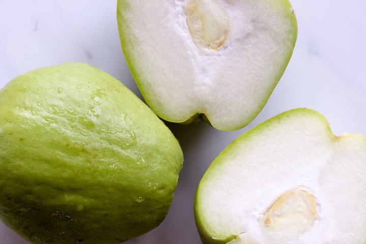 One whole chayote squash, one chayote squash cut in half, close up photo