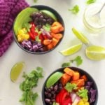 Bowl of mexican roasted sweet potatoes, black beans, red pepper, corn, avocado, limes and cilantro.