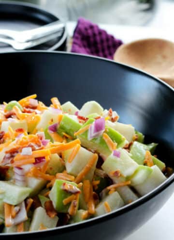 Large black bowl full of creamy chayote squash salad with bacon, cheddar cheese and onions