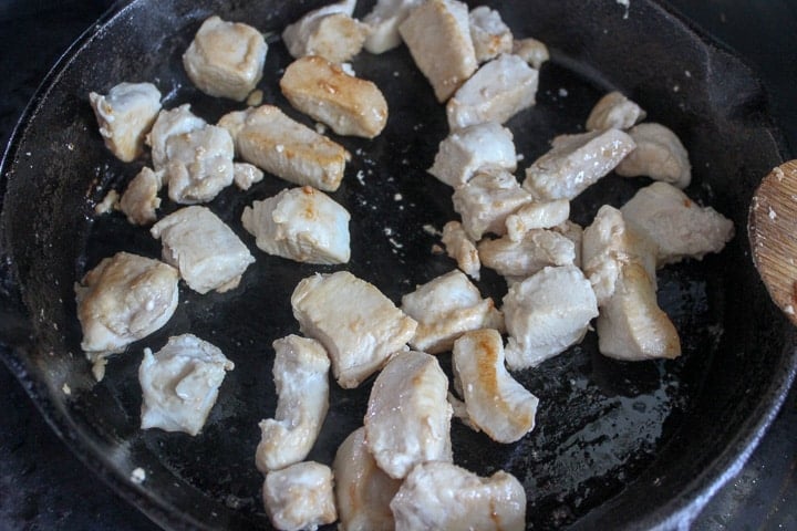 Chunks of chicken searing in a frying pan
