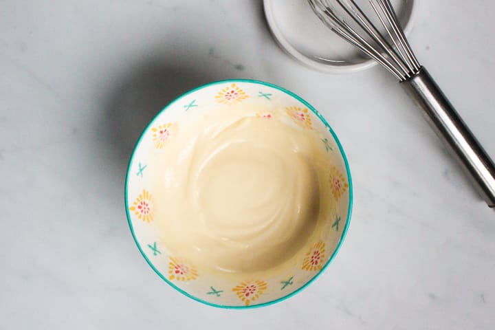 Bowl of creamy maple salad dressing on a marble counter.