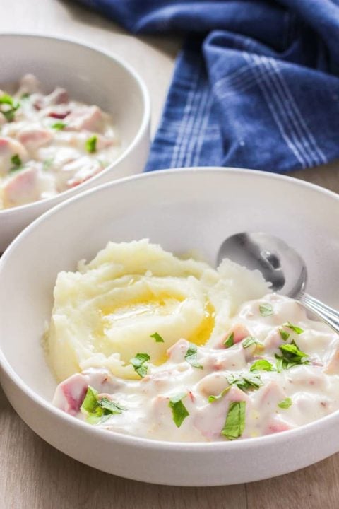 Bowl of mashed potatoes and ham in white bowl.