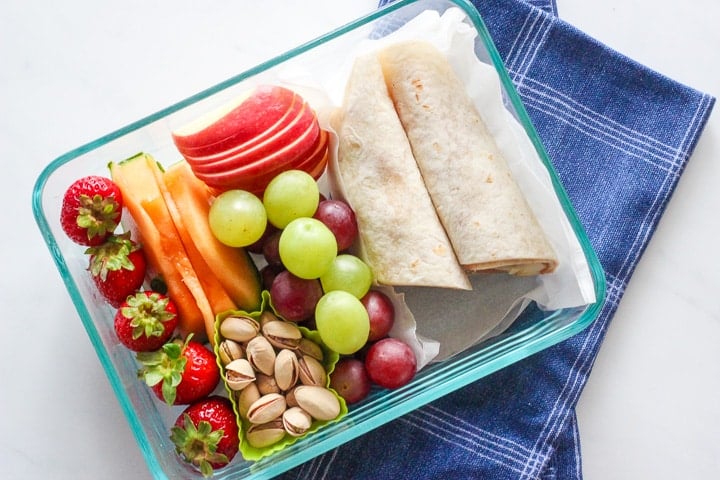 Dish of apples, strawberries, grapes, pistachios and a banana peanut butter wrap