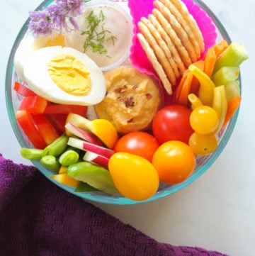 Dish with hardboiled egg, rice crackers, cherry tomatoes, carrot sticks, fresh green and yellow beans, hummus and ranch dip