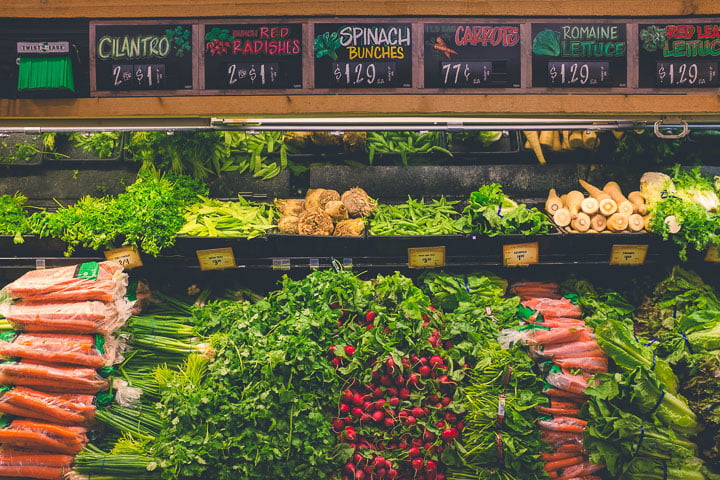 Grocery store shelves with fresh vegetables - carrots, herbs, radishes, lettuce