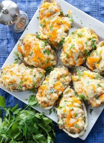 Baked potatoes covered in cheese and parsley on serving plate