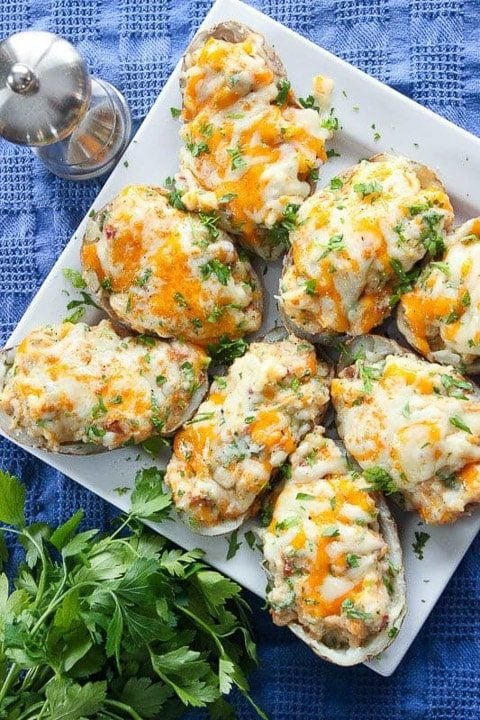 Baked potatoes covered in cheese and parsley on serving plate