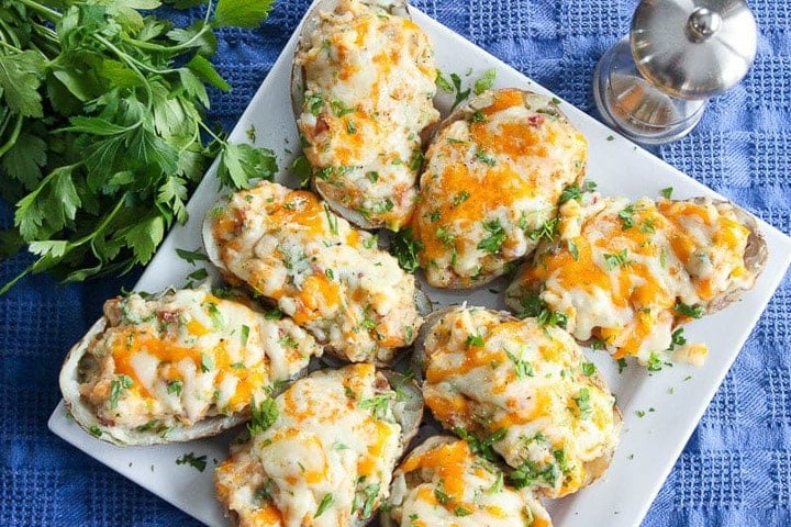 Twice baked potatoes covered in cheese and parsley on serving plate