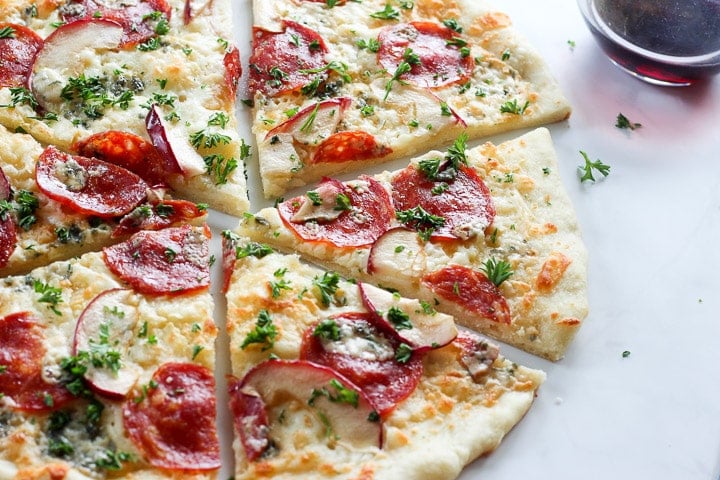 Thin crust pizza with salami, apple, parsley, blue cheese and glass of wine