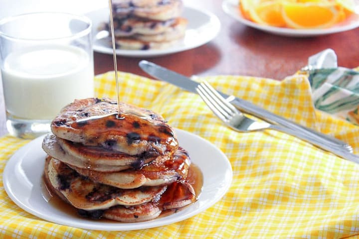 Stack of blueberry pancakes and glass of milk on yellow checkered table cloth