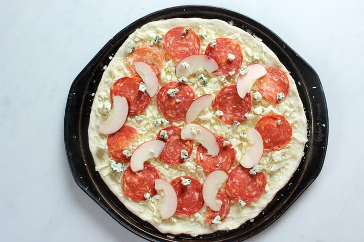 Uncooked pizza with salami, apple, blue cheese in pan