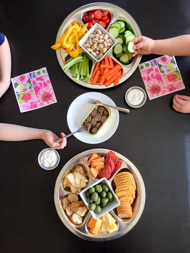 Plates of food including cut up vegetables, crackers, cheese and smoked oysters with kids eating
