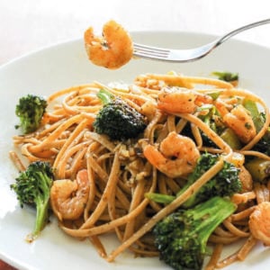 Pasta topped with shrimp and broccoli in white plate.
